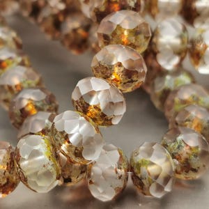 May include: Close-up of a strand of faceted beads. The beads have a mix of clear, gold, and brown tones, with a textured, geometric surface. The beads are strung together, creating a curved shape.