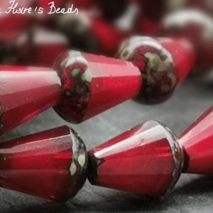 Könnte beinhalten: Nahaufnahme einer roten Glasperlenkette. Die Perlen sind kegelförmig und haben eine glänzende Oberfläche.