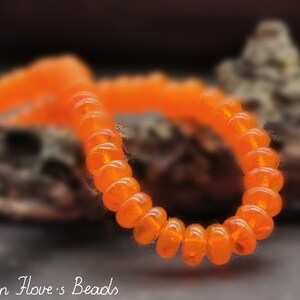 May include: A close-up of a bright orange beaded bracelet. The beads are small and round, and they are strung together to form a continuous loop. The bracelet is lying on a dark surface.