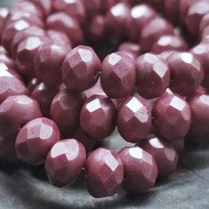 Könnte beinhalten: Nahaufnahme einer Kette aus facettierten, burgunderfarbenen Perlen. Die Perlen haben ein geometrisches, facettenreiches Design, das das Licht reflektiert. Die Perlen sind aneinandergereiht und bilden eine kreisförmige Form. Die Perlen haben eine tiefe, satte Farbe.