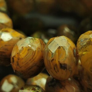 May include: Close-up of a strand of brown and gold gemstone beads. The beads are faceted and have a translucent appearance.