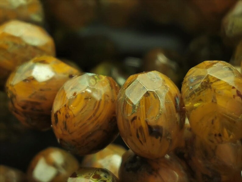 May include: Close-up of a strand of brown and gold gemstone beads. The beads are faceted and have a translucent appearance.