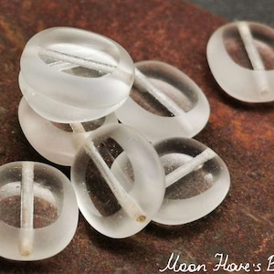 Peut inclure: Un groupe de sept perles en verre transparent avec une finition givrée. Chaque perle a une ligne blanche qui traverse le centre.