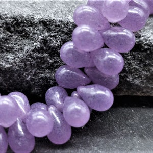 Puede incluir: Una hebra de cuentas de color lavanda en forma de lágrima. Las cuentas están hechas de vidrio o piedra preciosa y tienen un acabado liso y pulido.