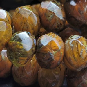 May include: A close-up of a strand of brown and gold faceted glass beads. The beads have a marbled effect and are translucent.