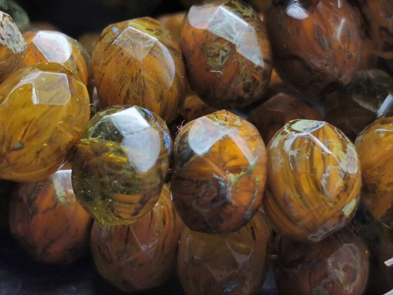 May include: A close-up of a strand of brown and gold faceted glass beads. The beads have a marbled effect and are translucent.