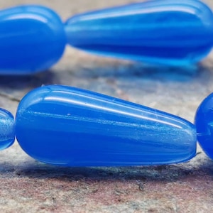 May include: A strand of bright blue glass beads in a teardrop shape. The beads have a translucent quality and a slight shimmer.
