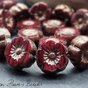 Könnte beinhalten: Nahaufnahme von mehreren dunkelroten, blütenförmigen Perlen mit goldenen Akzenten. Die Perlen haben ein detailliertes Blumendesign und sind eng aneinandergereiht. Der Text "Moon Flare's Beads" ist kursiv am unteren Rand geschrieben.