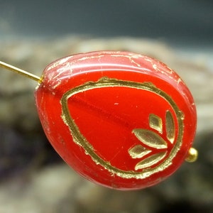 Puede incluir: Una cuenta de vidrio roja con un diseño de hoja de oro. La cuenta tiene forma de lágrima y tiene un acabado brillante.