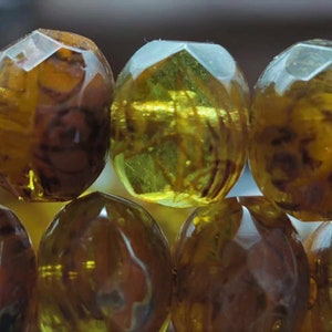 May include: A strand of amber-colored glass beads with a faceted design. The beads are translucent and have a warm, golden hue.