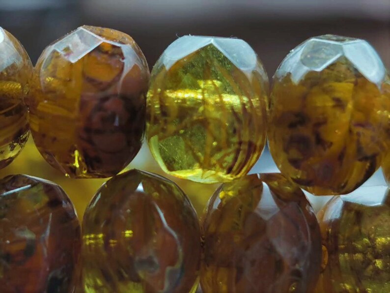 May include: A strand of amber-colored glass beads with a faceted design. The beads are translucent and have a warm, golden hue.