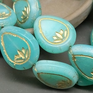 Puede incluir: Cuentas de vidrio azul turquesa con un diseño de hoja de oro. Las cuentas tienen forma de lágrima y un acabado ligeramente iridiscente.