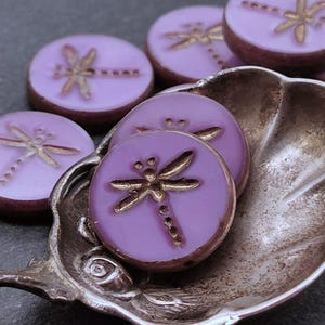 May include: Purple glass beads with a gold dragonfly design. The beads are round and have a smooth, glossy finish.