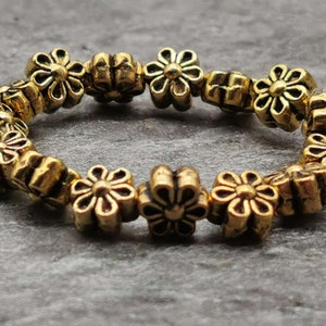 May include: A gold-toned bracelet made of small flower-shaped beads. The bracelet is made of metal and has a simple design.