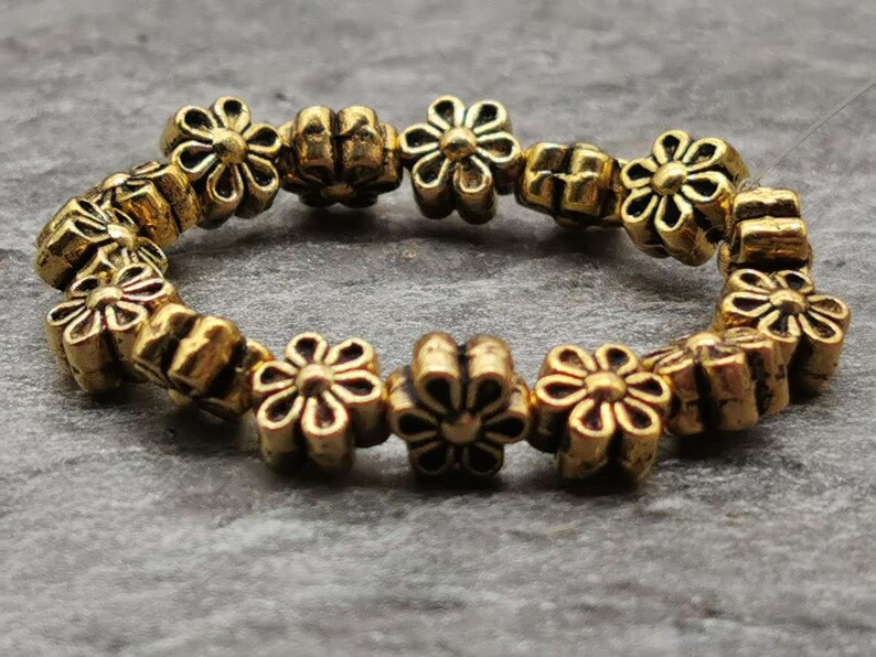 May include: A gold-toned bracelet made of small flower-shaped beads. The bracelet is made of metal and has a simple design.
