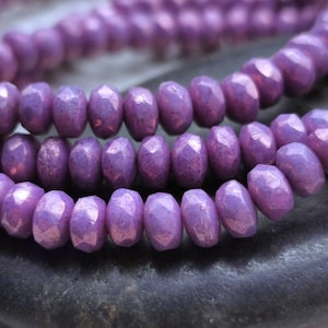 May include: A strand of iridescent purple faceted glass beads. The beads are small and have a slightly irregular shape.