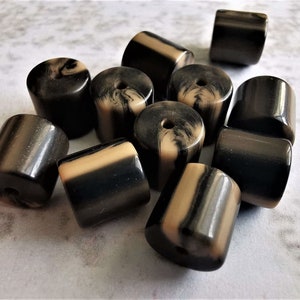 Könnte beinhalten: Eine Gruppe von 12 schwarzen und weißen, gestreiften, zylindrischen Perlen. Die Perlen sind aus einem glatten, glänzenden Material gefertigt und haben ein Loch in der Mitte.