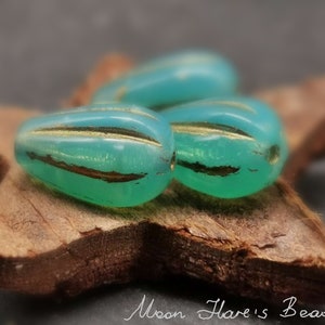 Peut inclure: Trois perles en verre bleu turquoise avec des accents dorés. Les perles sont en forme de larme et ont une finition brillante.
