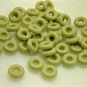 Könnte beinhalten: Ein großer Haufen hellgrüner donutförmiger Perlen. Die Perlen sind aus einem glatten, glänzenden Material gefertigt.