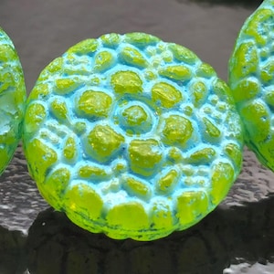 以下が含まれることがあります： 3つの丸くテクスチャ加工されたオブジェクトのクローズアップ。オブジェクトは、ライムグリーンとライトブルーの組み合わせで、鮮やかな配色です。表面は、ユニークな視覚的テクスチャを作成する、でこぼこの有機的なパターンを持っているようです。オブジェクトはおそらく装飾的または芸術的です。