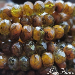 May include: A strand of faceted glass beads in shades of brown, green, and gold. The beads have a marbled or swirled appearance.