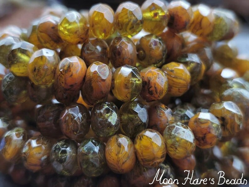 May include: A strand of faceted glass beads in shades of brown, green, and gold. The beads have a marbled or swirled appearance.