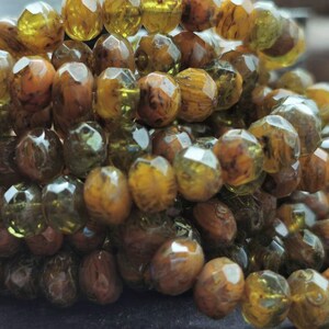 May include: A strand of faceted glass beads in shades of brown and green. The beads have a unique marbled effect, creating a natural and organic look.