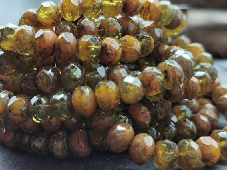 May include: A strand of faceted glass beads in shades of brown and green. The beads have a unique marbled effect, creating a natural and organic look.