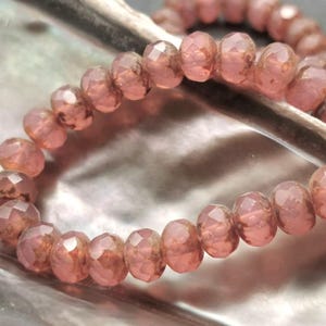 May include: A strand of pink faceted glass beads. The beads are strung on a clear thread and are arranged in a circular pattern.