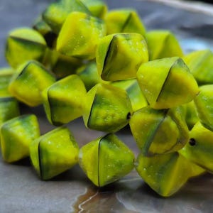 May include: A close-up of a strand of yellow and green glass beads. The beads are faceted and have a diamond shape. The beads are strung on a clear thread.