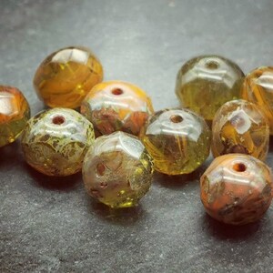 May include: A collection of ten faceted glass beads in shades of green, yellow, and orange. The beads have a mottled, marbled appearance.