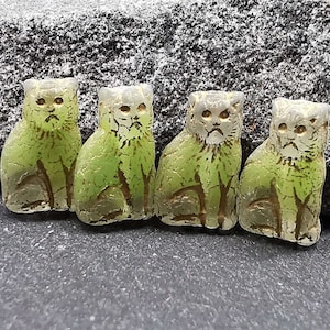 Puede incluir: Cuatro figuritas de gato de vidrio verde con detalles blancos. Los gatos están sentados con sus colas enroscadas alrededor de sus patas.