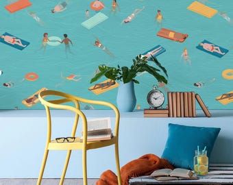 May include: A yellow chair with a book and glasses on it sits in front of a blue wall with a wallpaper depicting a beach scene with people swimming and floating on inflatable rafts. A wooden pallet with a blanket and a glass of lemonade sits on the floor.