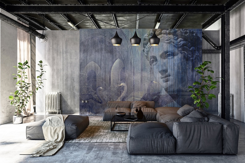 May include: A modern living room with a gray sectional sofa, a coffee table, and two potted plants. The wall behind the sofa features a large mural with a blue and white abstract design and a woman's face.