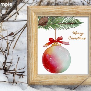 Puede incluir: Una pintura de acuarela de un adorno navide&ntilde;o colgando de una rama de pino. El adorno es rojo, blanco y verde con una parte superior dorada. El texto "Merry Christmas" est&aacute; escrito en letras doradas sobre un fondo blanco.