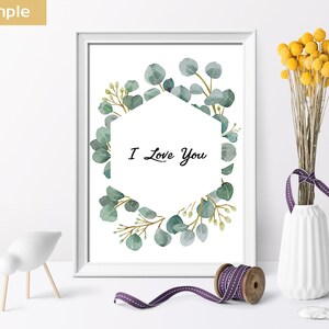 May include: A white framed print with a watercolor illustration of a eucalyptus wreath surrounding a hexagon with the text "I Love You".