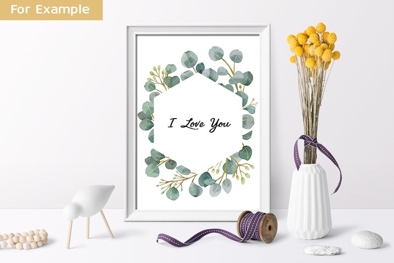 May include: A white framed print with a watercolor illustration of a eucalyptus wreath surrounding a hexagon with the text "I Love You".