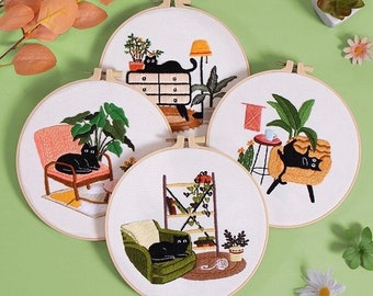 Può includere: Quattro cerchi da ricamo con disegni di gatti neri, piante e mobili. I cerchi sono su uno sfondo verde. Il testo "HANDMADE PLEASURE" è scritto nella parte superiore dell'immagine.