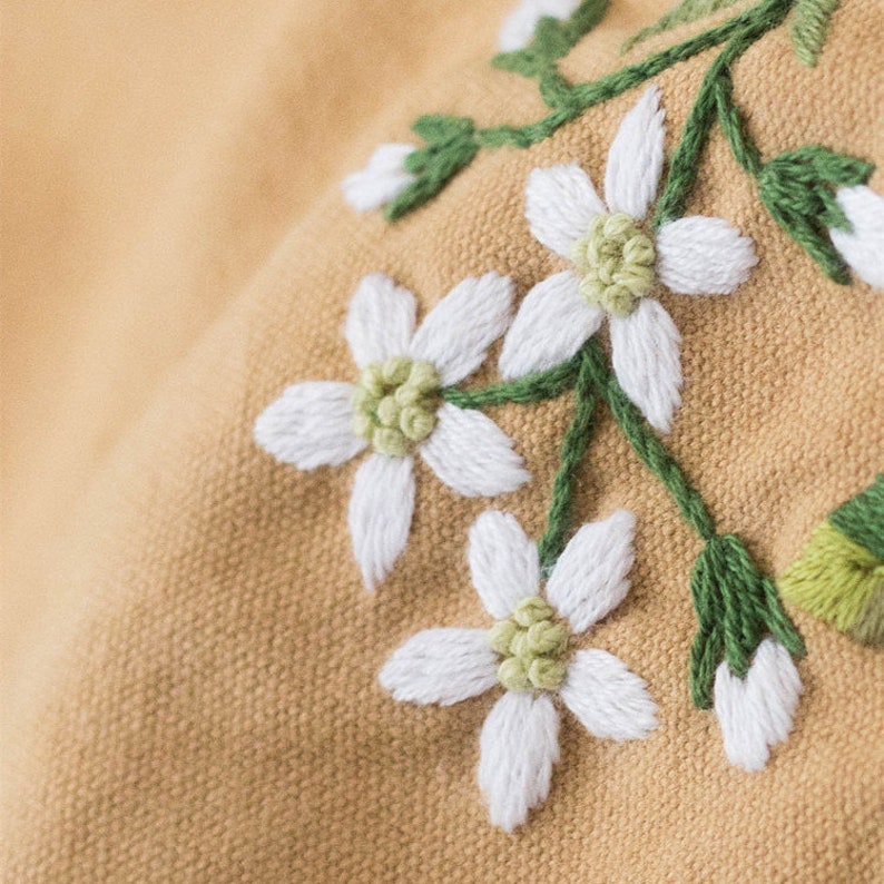 May include: Close-up of embroidered white flowers with green stems on a light brown fabric.
