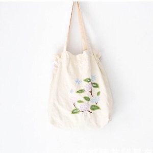 May include: A white canvas tote bag with a floral embroidery design. The embroidery features pink and blue flowers with green leaves.