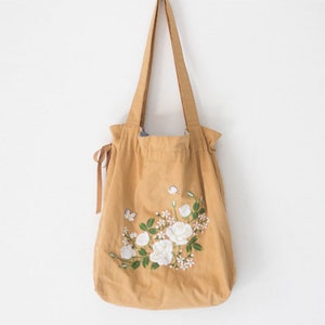 May include: A mustard yellow canvas tote bag with white embroidered flowers and butterflies.