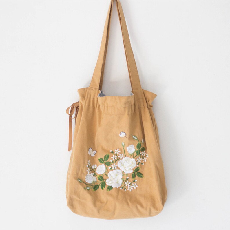May include: A mustard yellow canvas tote bag with white embroidered flowers and butterflies.