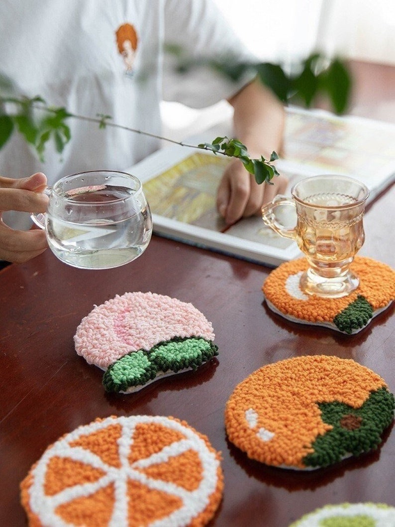 May include: Set of six colorful fruit-shaped coasters. The coasters are made of a fluffy, textured material and feature a variety of fruits, including oranges, lemons, and peaches.
