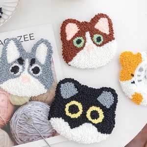 May include: Three colorful cat-shaped punch needle kits. The cats are brown and white, gray and white, and black and white. Each kit includes a pre-punched canvas, yarn, and a needle.