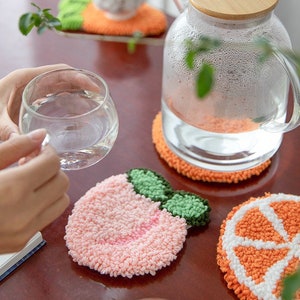 May include: Set of four colorful crocheted coasters featuring a peach, orange slice, and two orange halves. The coasters are made with a fluffy yarn and are perfect for protecting surfaces from heat and spills.