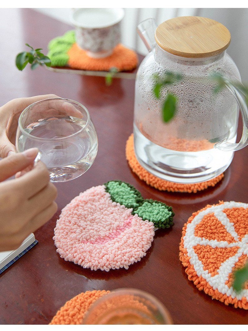 May include: Set of four colorful crocheted coasters featuring a peach, orange slice, and two orange halves. The coasters are made with a fluffy yarn and are perfect for protecting surfaces from heat and spills.
