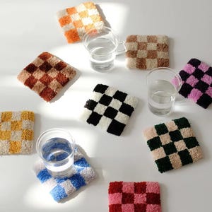May include: Set of 8 colourful checkered coasters made of fluffy fabric. The coasters are in various colours, including black, white, pink, red, green, blue, orange, and brown.