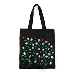 May include: Black tote bag with embroidered floral design. The flowers are white, yellow, and purple with green stems and leaves. The tote bag has a rectangular shape and two black handles.