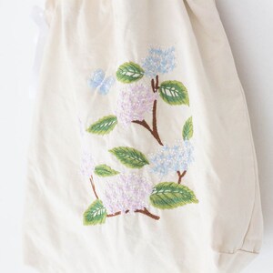 May include: A white canvas tote bag with an embroidered design of pink, blue, and green hydrangeas and a butterfly.