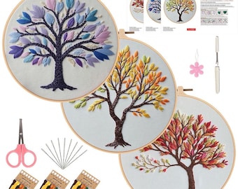 May include: Embroidery DIY art kit featuring three completed tree designs in wooden hoops. The trees display colorful leaves in shades of blue, yellow, orange, and red. Additional supplies include scissors, needles, and thread.